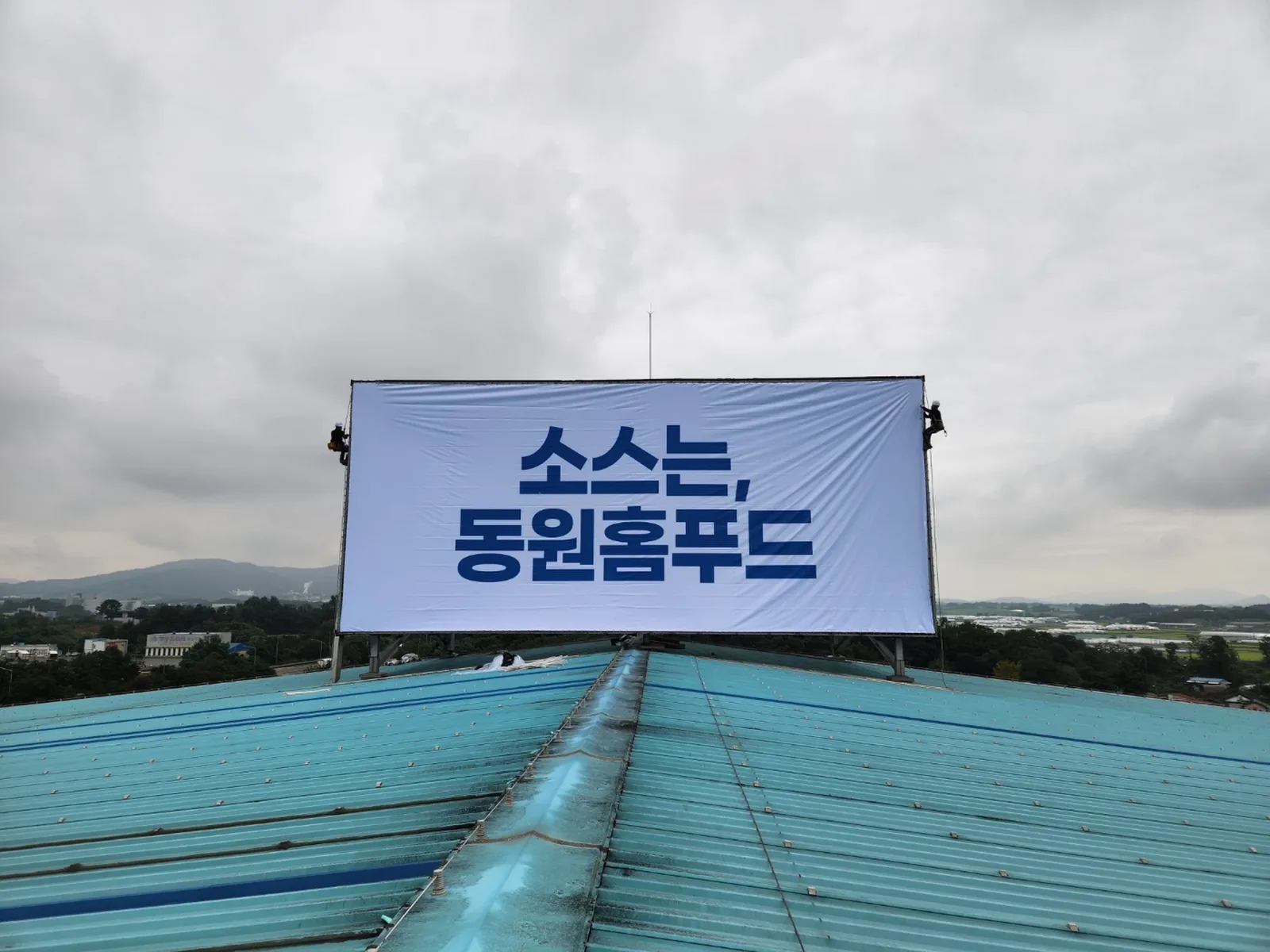 동원홈푸드 옥상광고탑 현수막 교체 설치 후, 로프 작업자가 원단을 팽팽하게 고정한 완성 현장