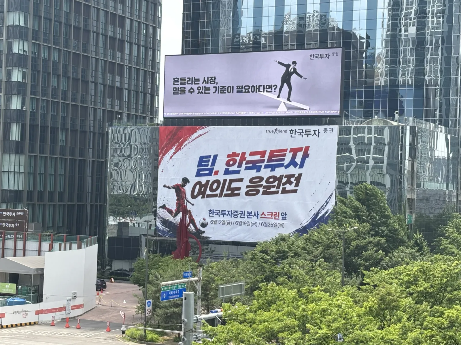 로프 고공 작업자가 설치한 건물 외벽 현수막, 조경수와 함께 보이는 시공 현장